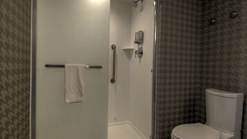 A bathroom with a glass-enclosed shower, a towel rack, a toilet, and patterned wallpaper.