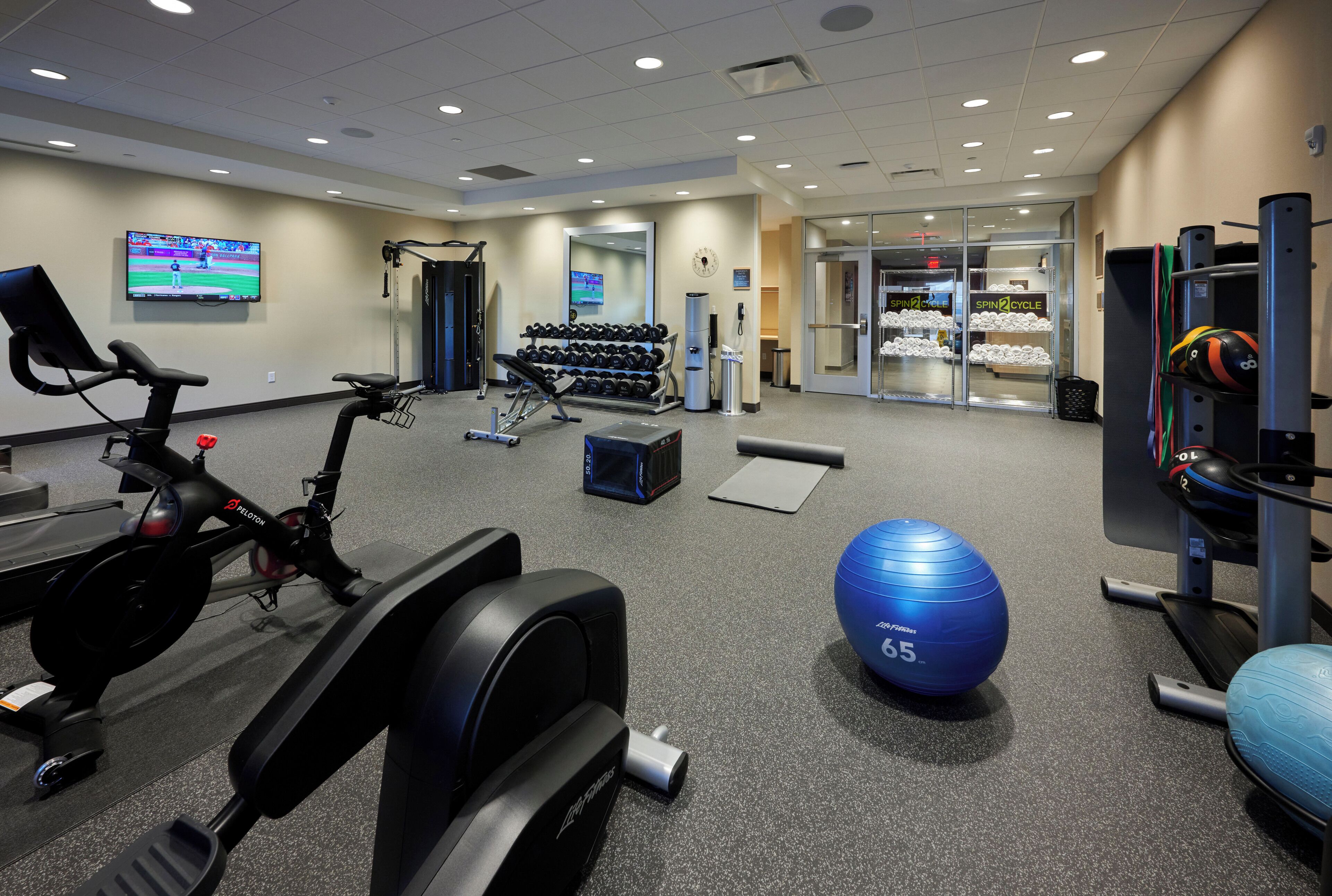 A gym with cardio equipment, dumbbells, a blue exercise ball, and a water station.