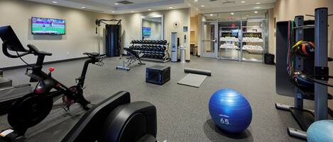 Un gimnasio con equipo cardiovascular, mancuernas, una pelota de ejercicio azul y una estación de hidratación.