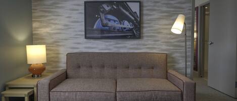 A hotel room with a grey sofa, a framed picture on the wall, and two lamps on side tables.