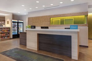 Zona de recepció d'hotel amb un disseny modern, que inclou un taulell de recepció, un minibar i una màquina de begudes a disposició del client.
