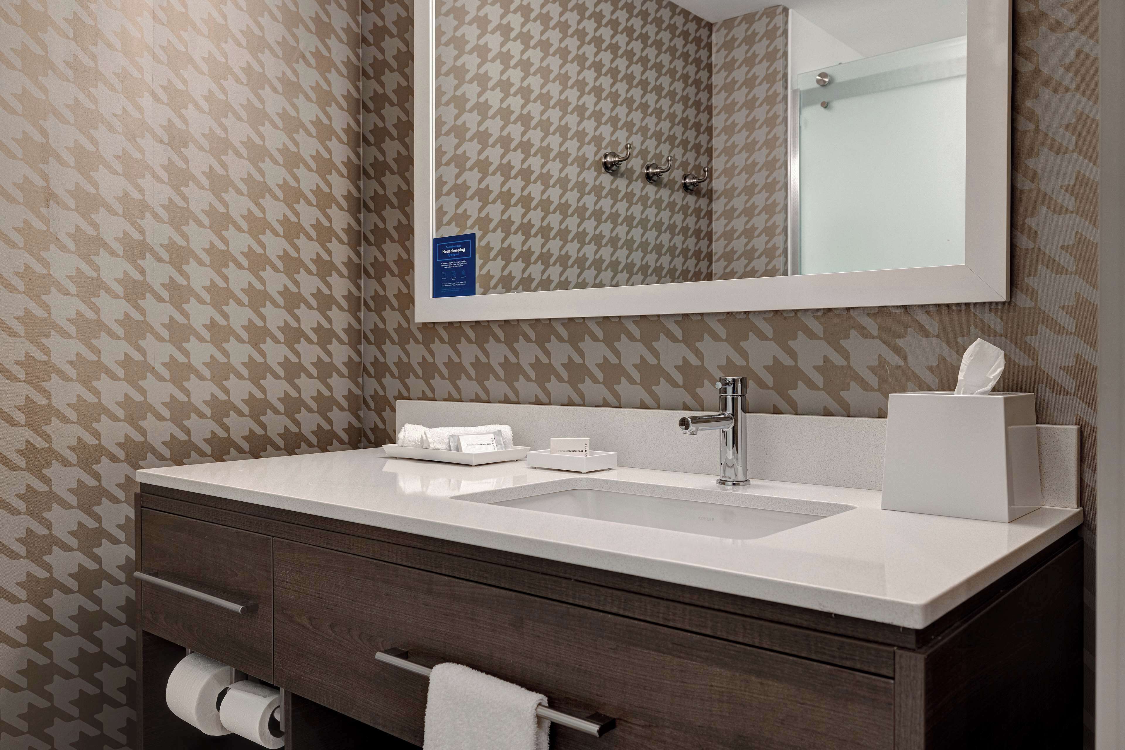 A bathroom with a large mirror, a sink, and a towel rack.