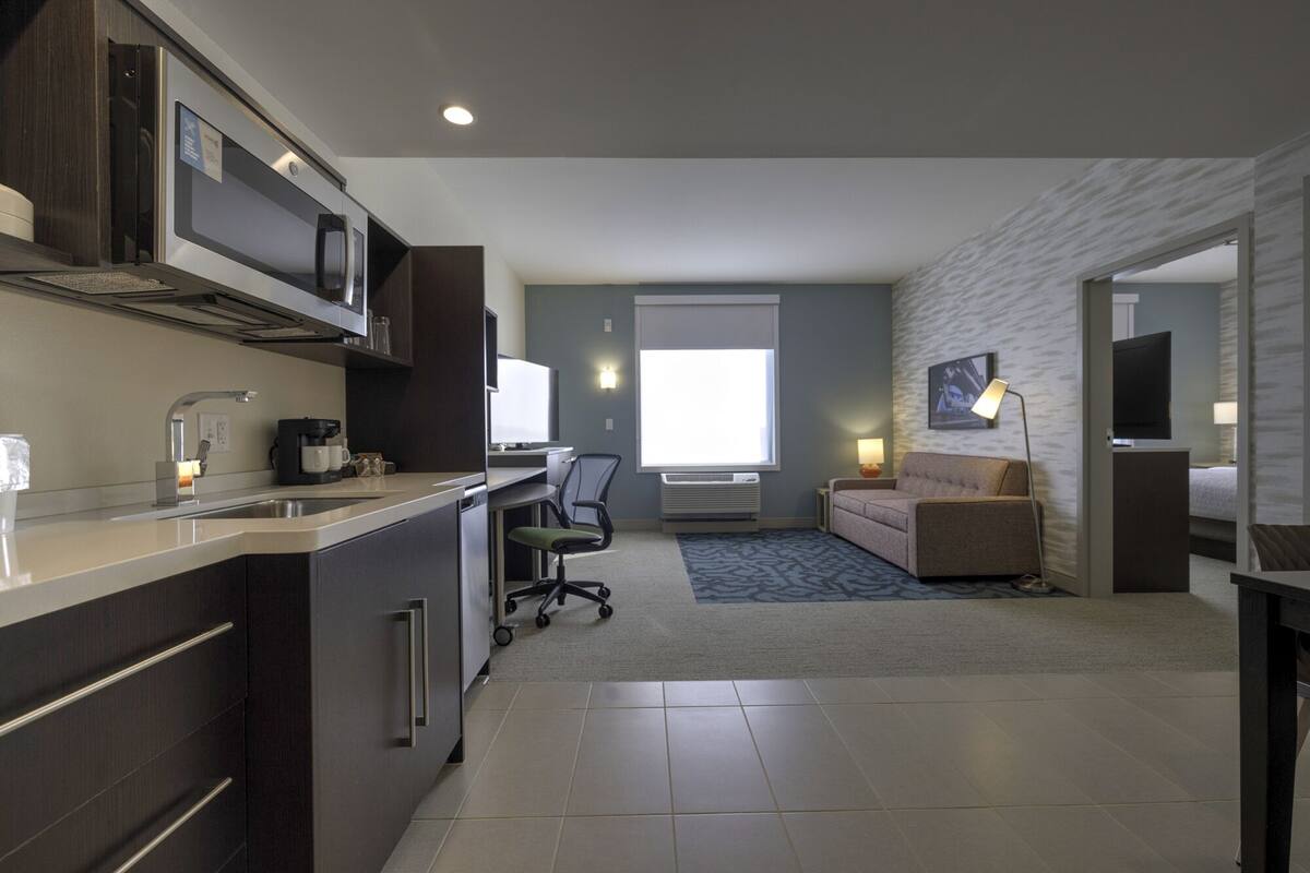 Une chambre d’hôtel moderne équipée d’une kitchenette, d’un canapé, d’une télévision et d’une lampe.