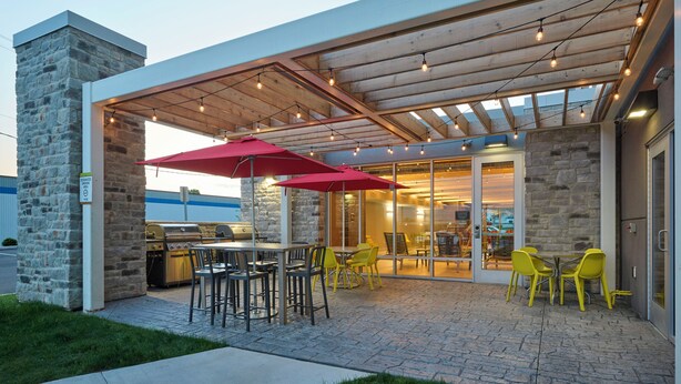 Eine Terrasse im Freien mit Steinmauern, einem Grill, gelben Stühlen und einem roten Sonnenschirm.