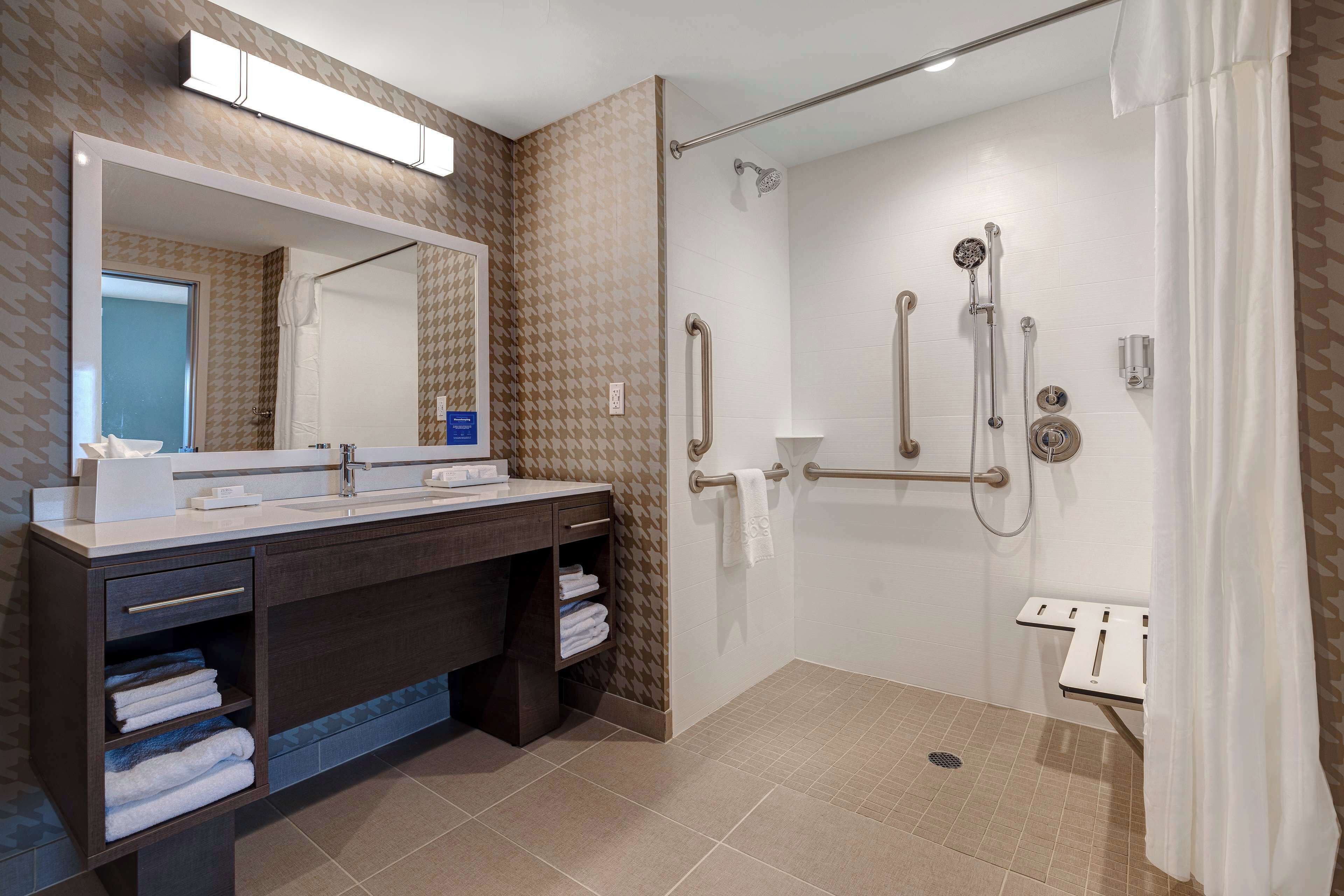 Un baño moderno con ducha a ras de suelo, tocador con espejo y un perchero para toallas.