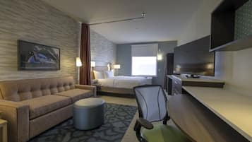 Et hotelværelse med seng, sofa, skrivebord, stol og fjernsyn.