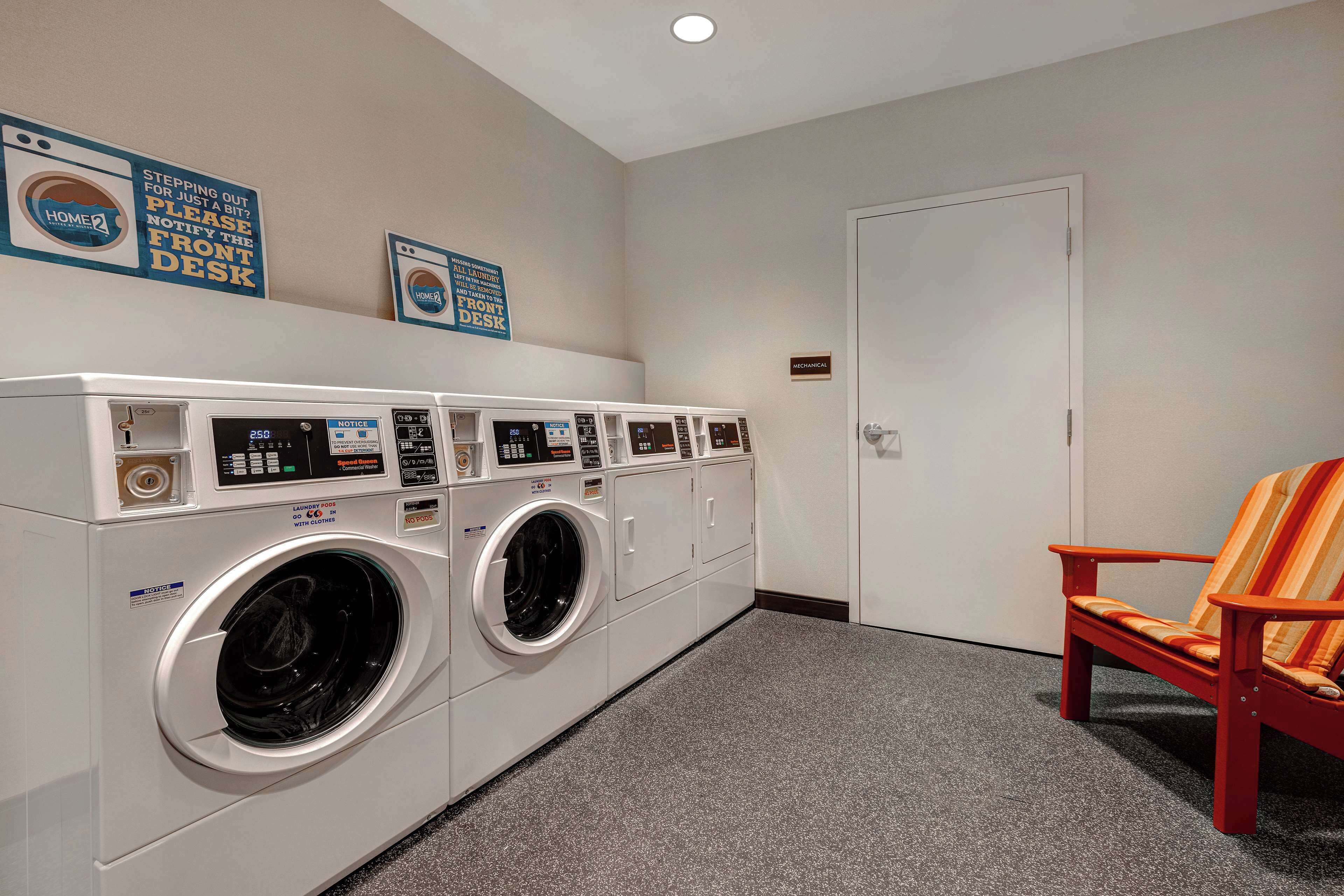 A laundry area with multiple washing machines, a chair, and signs on the wall.
