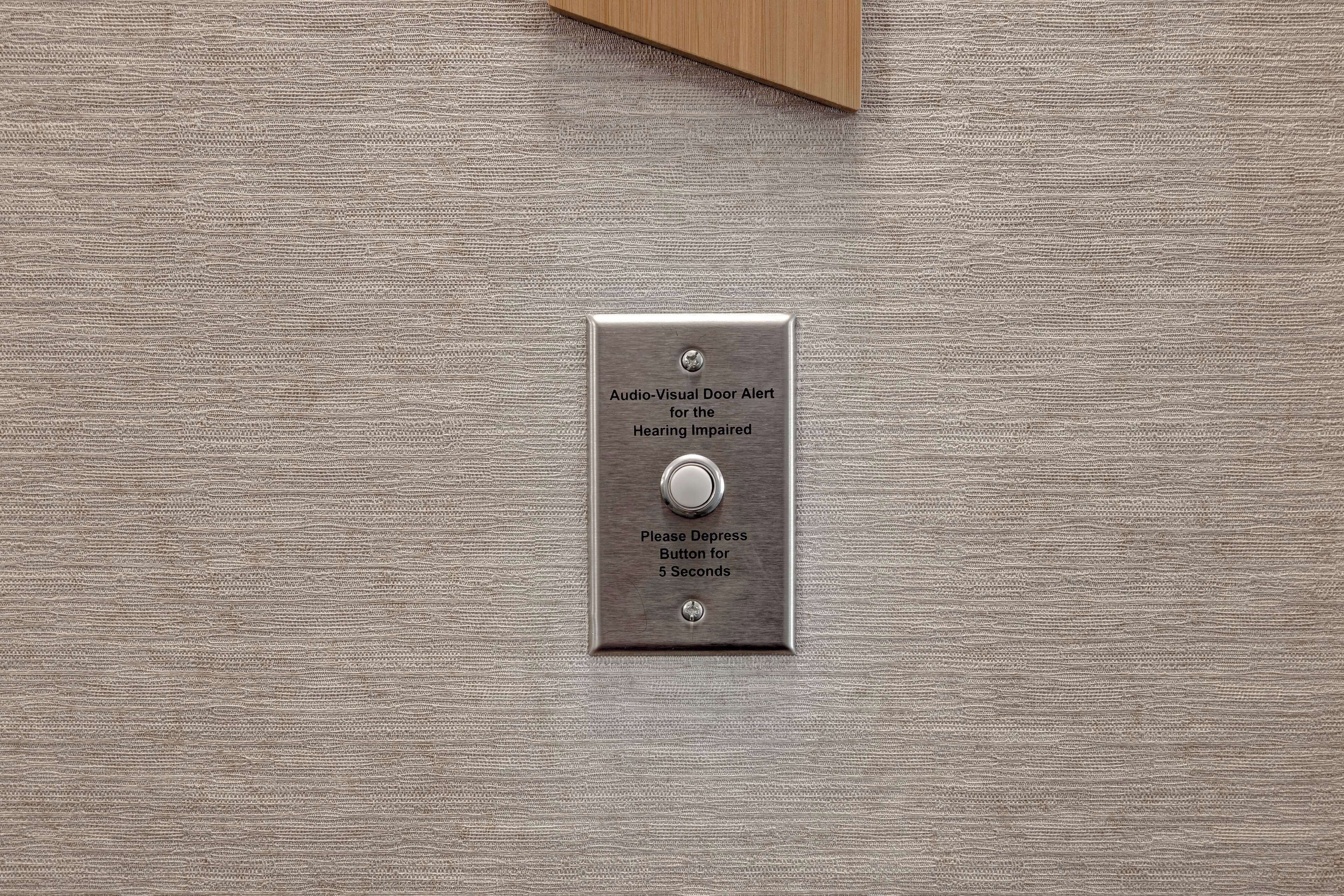 A metallic plate with a button and text indicating an audio-visual door alert system for the hearing impaired.