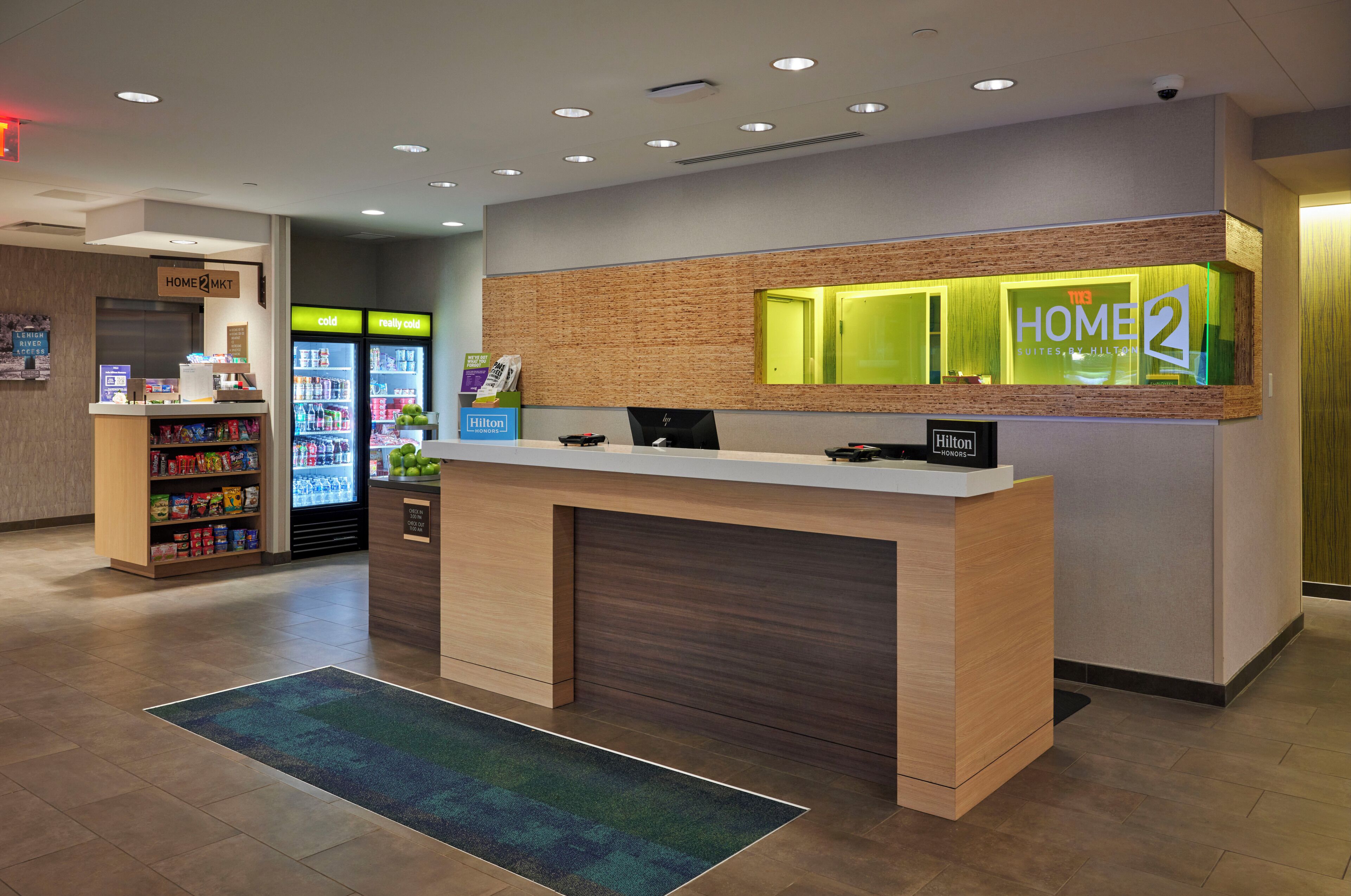 Zona de recepción de un hotel con mostrador, minibar, máquina expendedora y vitrina con el nombre del hotel.