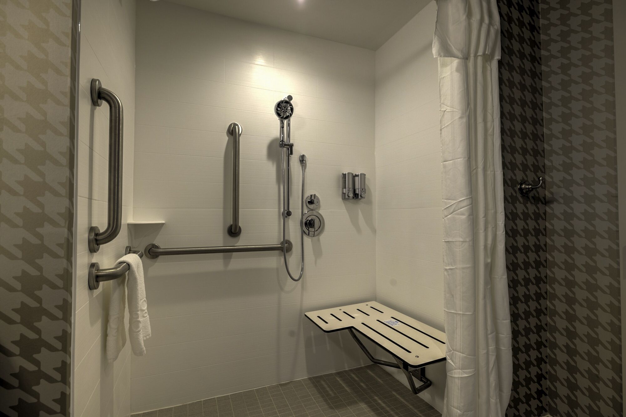 Ducha con barras de apoyo, cabezal de ducha manual y un asiento.