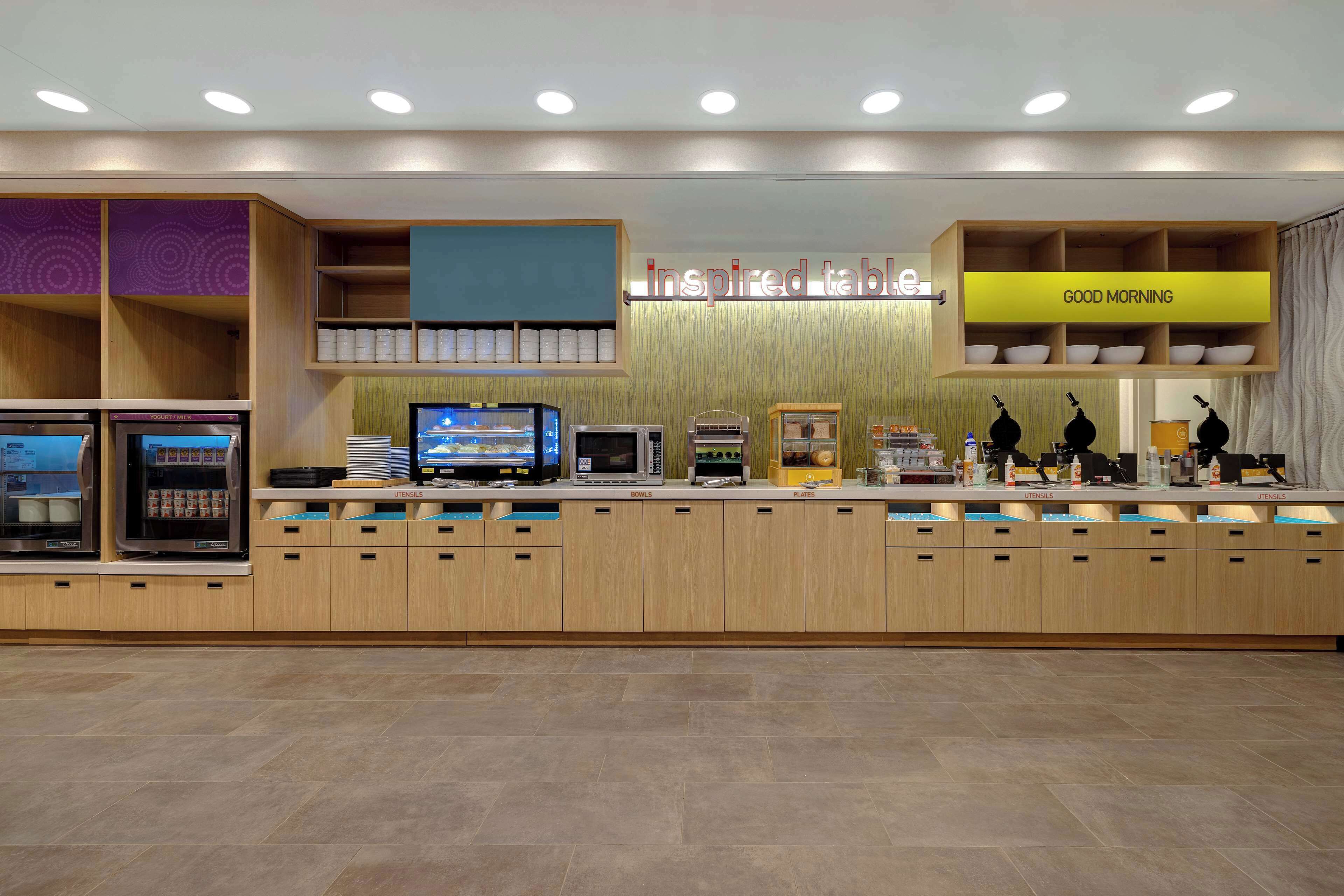 A modern kitchen area with a self-service station, including a coffee machine, microwave, and various utensils.