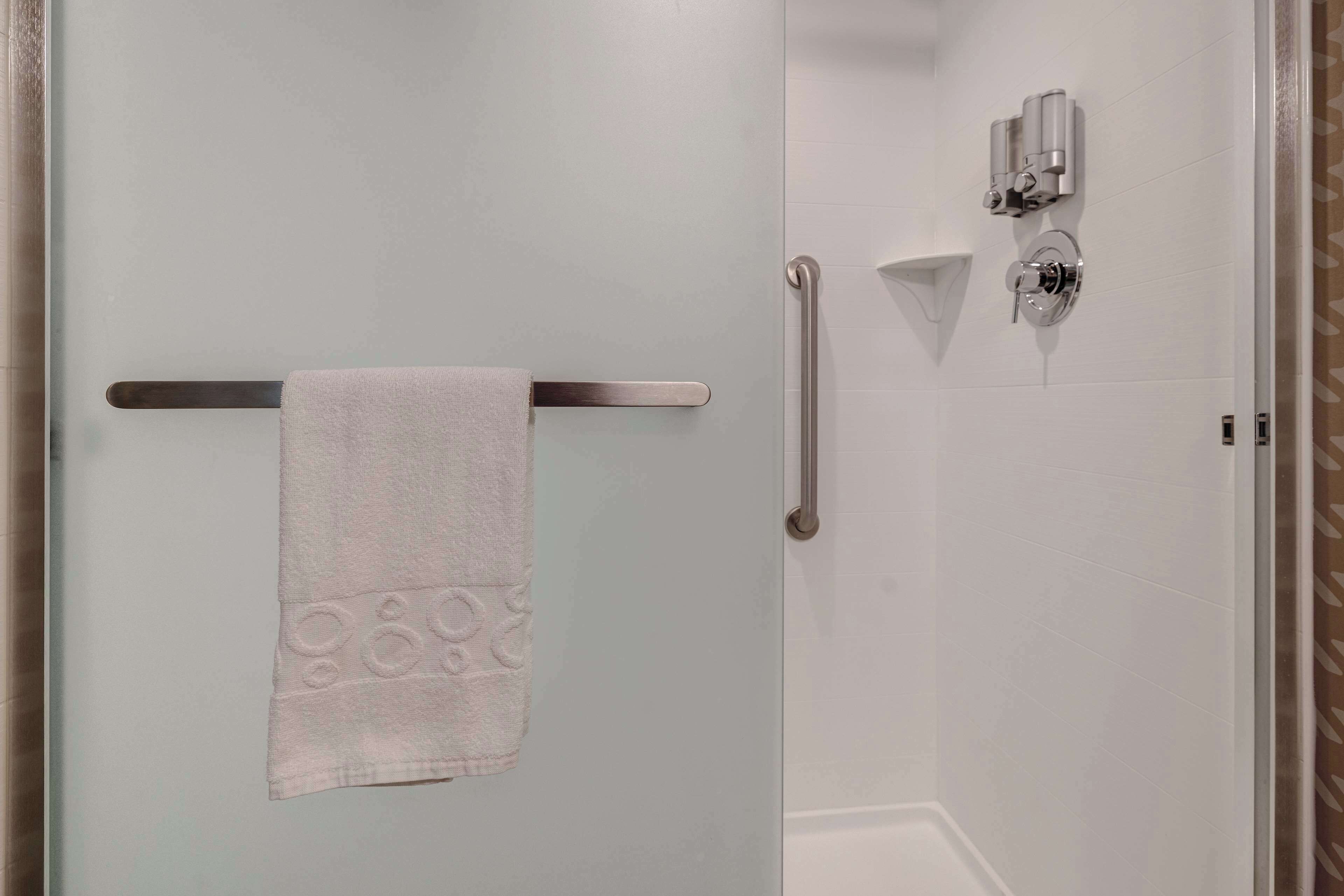 Un baño con toallero, barra de apoyo y cabezal de ducha.