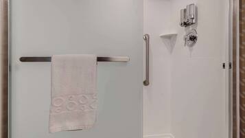 Un baño con toallero, barra de apoyo y cabezal de ducha.