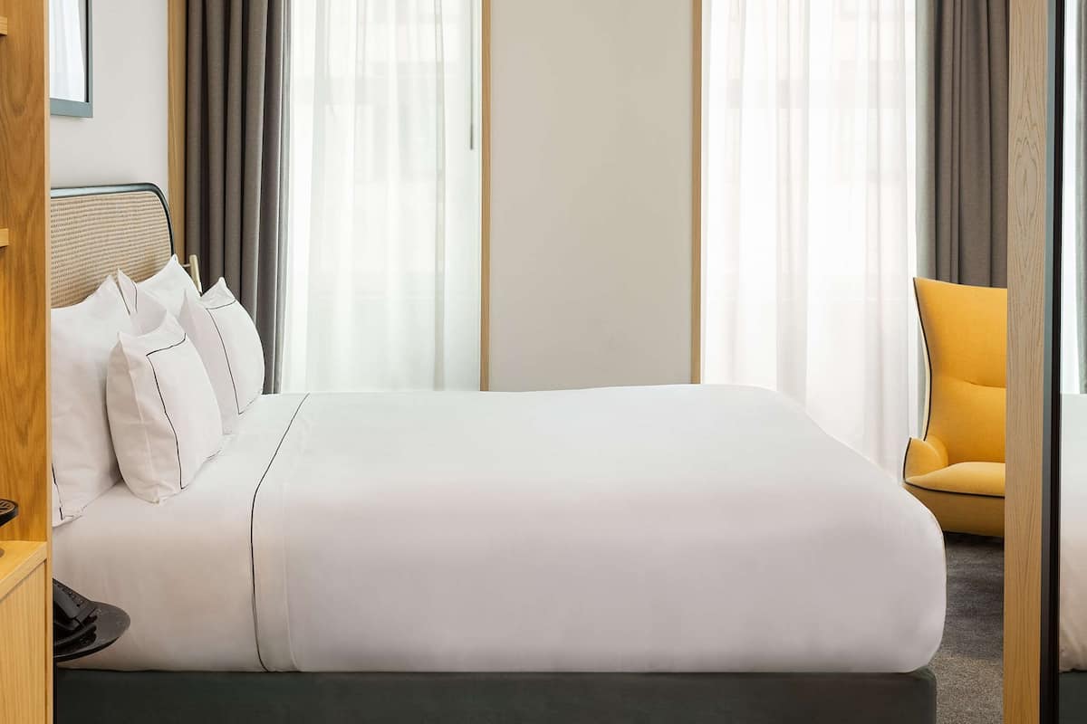 A hotel room with a large bed, a bedside table, a chair, and a window with curtains.