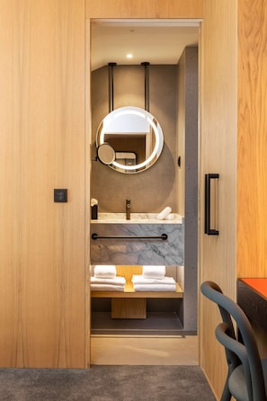 A modern bathroom with a wooden vanity, a marble countertop, a built-in sink, a towel rack, and a mirror with a circular light. - Arts Hotel Porto, Tapestry Collection By Hilton (Porto)