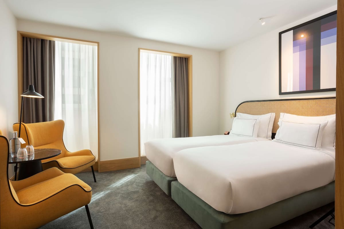 A hotel room with a double bed, two bedside tables, a chair, and a large window with curtains.