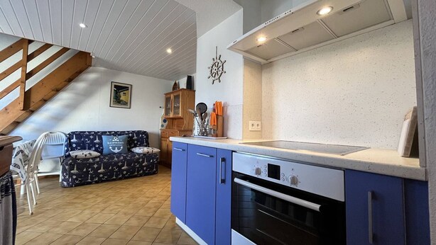 A modern kitchen with blue cabinets, a Bosch oven, and a wooden staircase leading to a living area with a patterned sofa. - Family home near beach in Saint-Denis d'Oléron, enclosed garden (Saint-Denis-d'Oléron)