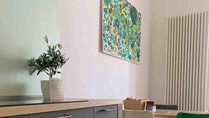 Eine moderne Küche mit grauen Schränken, einer Holzarbeitsplatte und einem Blumentopf. Es gibt eine Essecke mit einem weißen und einem grünen Stuhl, sowie ein farbenfrohes abstraktes Gemälde an der Wand.