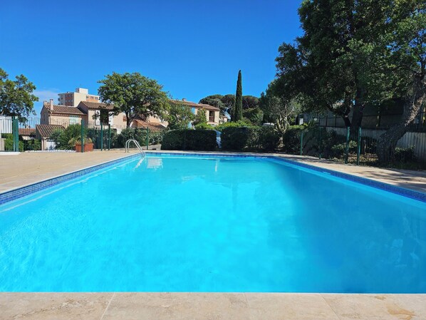 A clear blue swimming pool surrounded by a fence, with buildings and trees in the background. - Air-conditioned Provençal mazet for 10 people (Sainte-Maxime)
