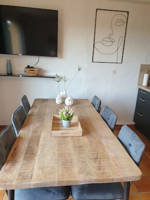 Een houten eettafel met een plant in het midden, omringd door grijze gestoffeerde stoelen.
