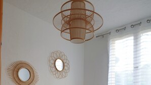 Ett sovrum med en sänggavel i trä, en stor säng med vita sängkläder, två väggspeglar och en taklampa av rotting.
