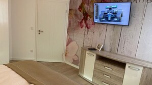 Ein Schlafzimmer mit einem Bett, einer Holzkommode und einem an der Wand montierten Fernseher, der ein Formel-1-Rennen zeigt.
