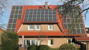 Ein Haus mit rotem Dach, Ziegelwänden und mehreren Solaranlagen auf dem Dach.