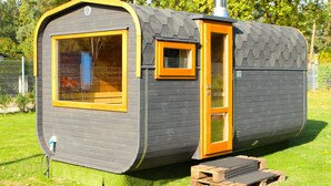 Une petite cabane à un seul étage, dotée d’une grande fenêtre et d’une porte attenante, située sur une pelouse, avec des arbres en arrière-plan.