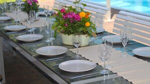 Une table à manger dressée pour un repas, avec de l’argenterie blanche, des couverts et des verres à vin, agrémentée d’un centre de table floral.