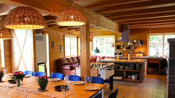 Un intérieur en bois comprenant un coin repas, des chaises bleues et une table de baby-foot.