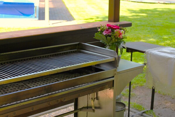 En grill med ett metallgaller, en metallbehållare och ett bord med ett vitt tygstycke på.
