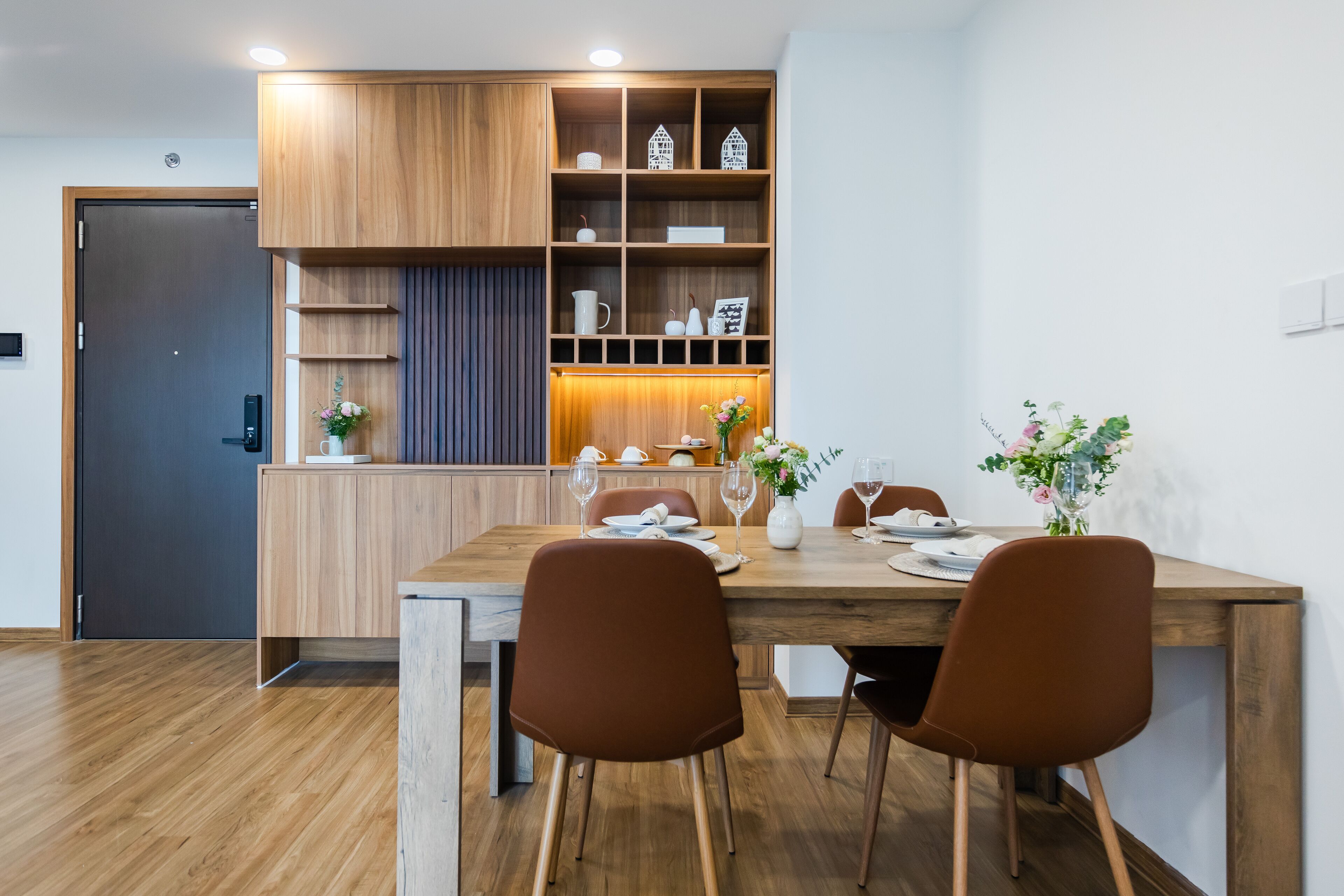 Un comedor moderno con una mesa de madera, sillas marrones y un armario empotrado de madera con estantes.