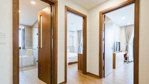 Quarto de hotel com chão de madeira, uma cama, uma escrivaninha com computador e um banheiro com chuveiro.