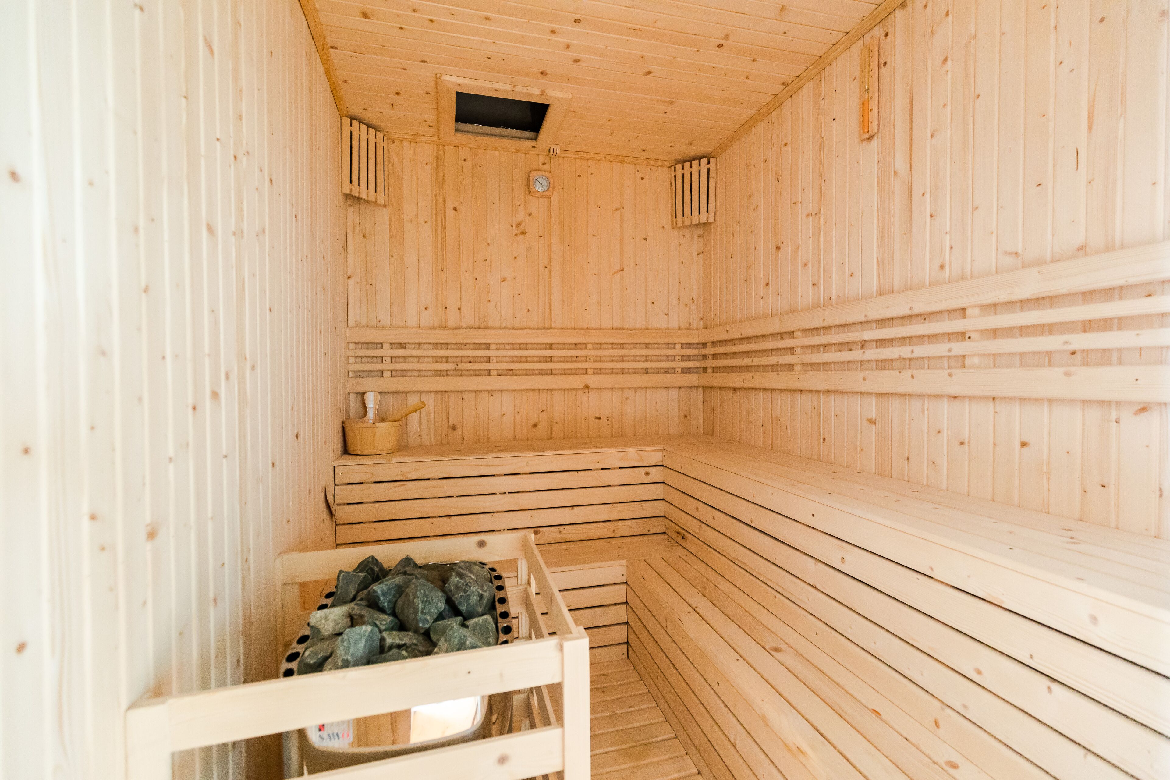 A sauna with wooden walls and benches, a small window, and a wooden bench with a towel and a bottle.