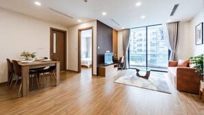 Uma sala de estar moderna com uma mesa de jantar de madeira, um sofá, uma televisão e uma janela grande com cortinas.