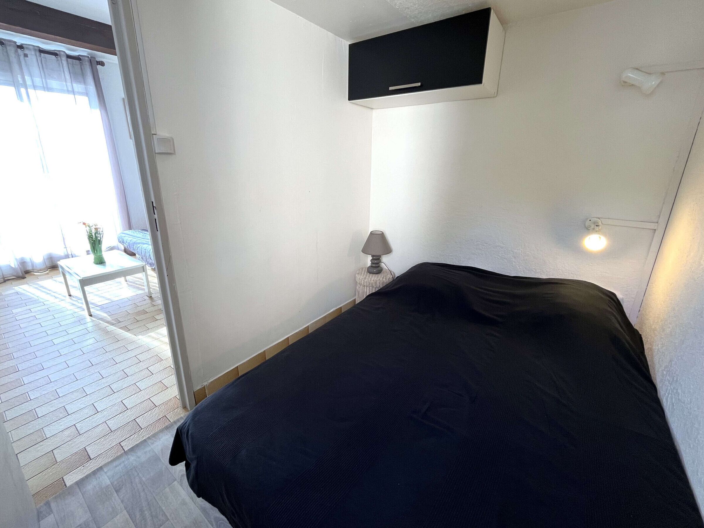 Une chambre à coucher comprenant un lit, une table de chevet avec une lampe, une fenêtre avec des rideaux et un climatiseur fixé au mur.