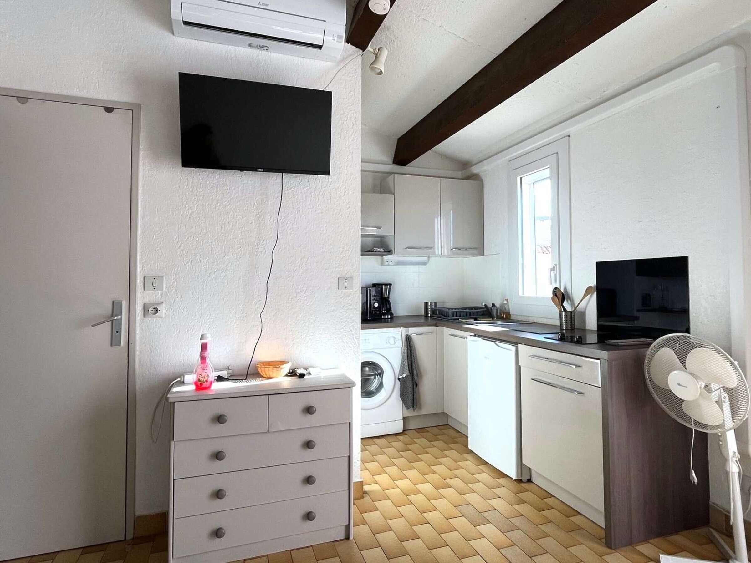 A compact kitchen with white cabinets, a washing machine, a coffee maker, and a fan.