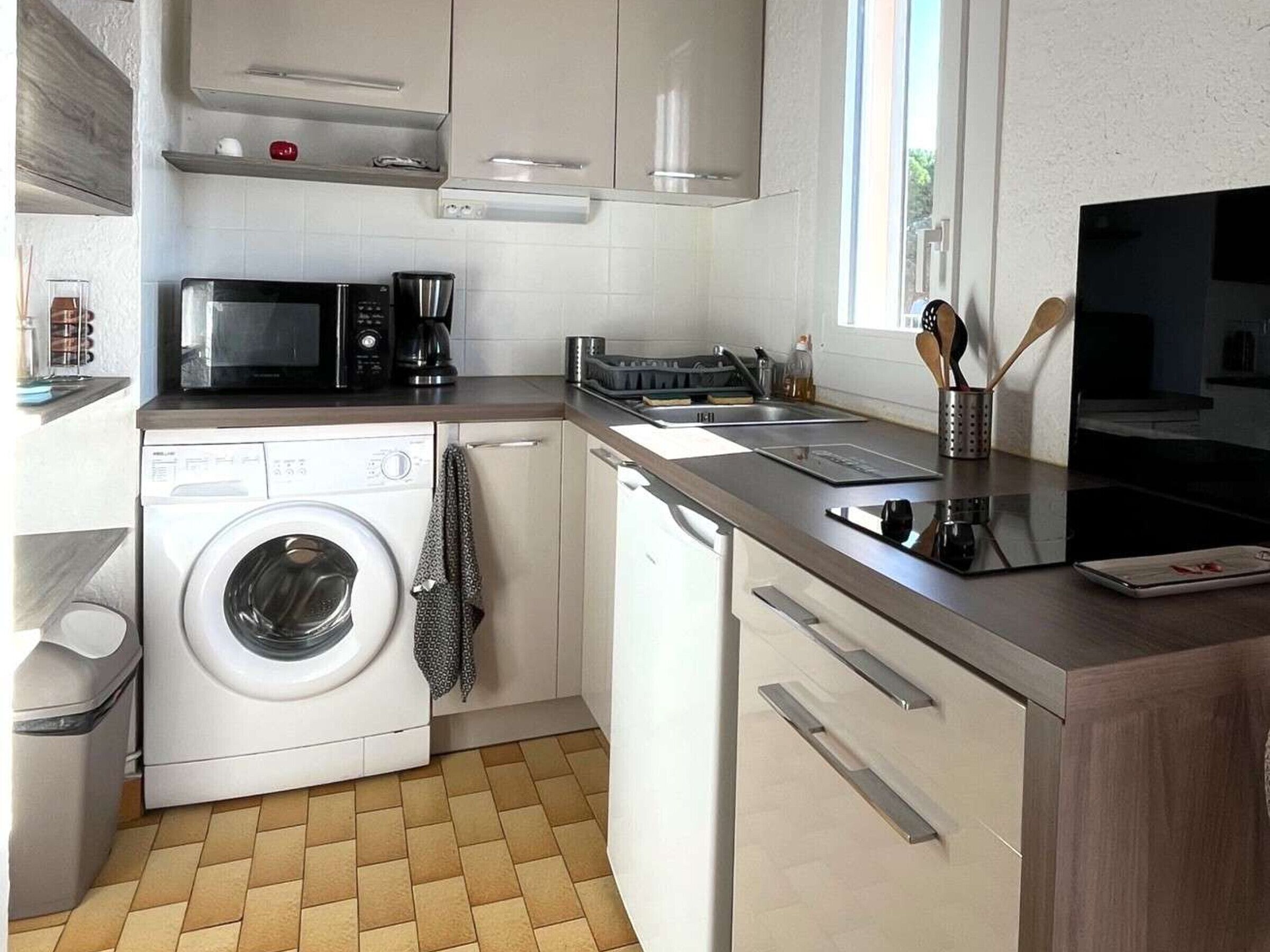 A compact kitchen with a washing machine, microwave, coffee maker, and a small window.