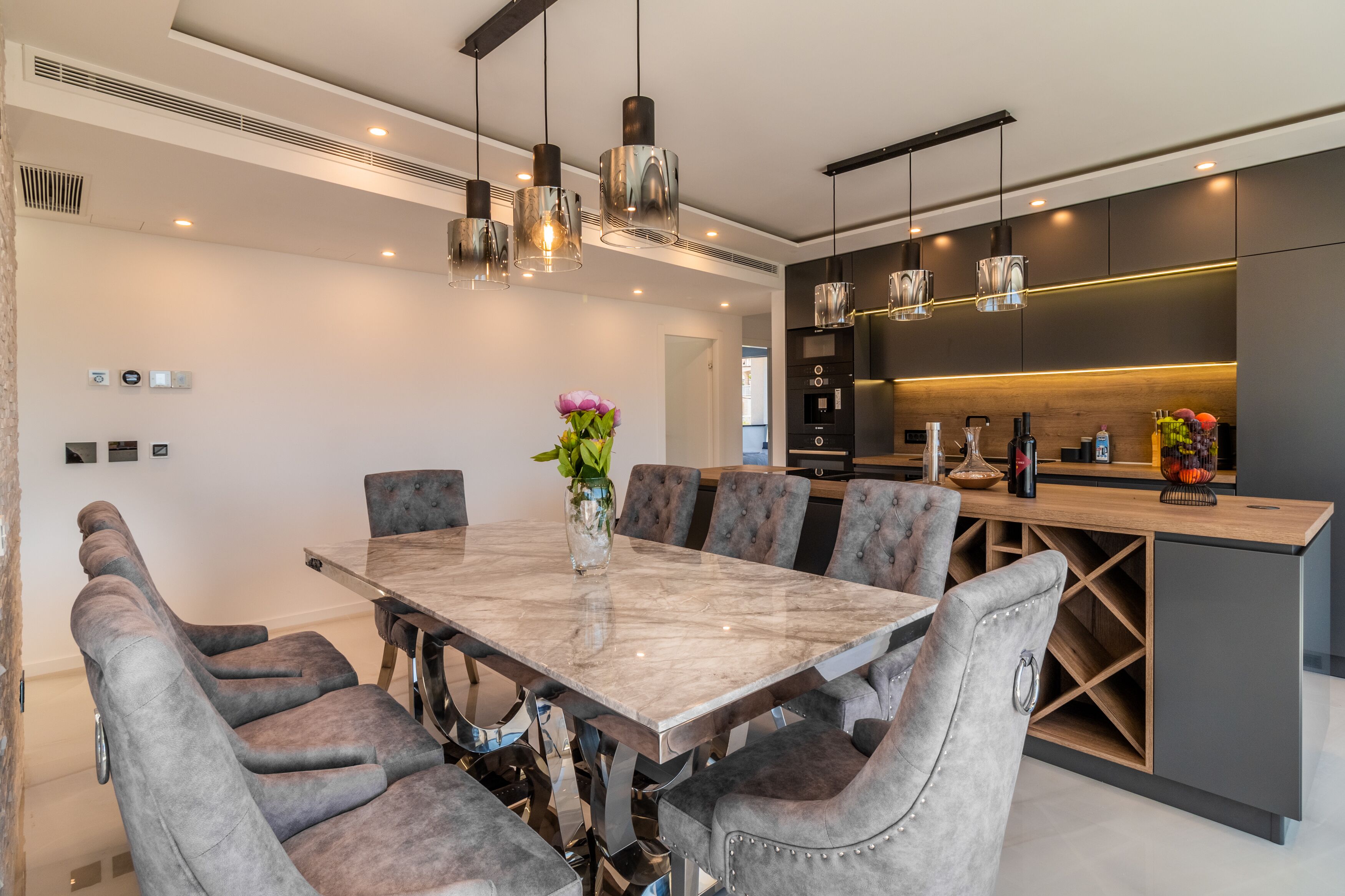 Une cuisine moderne dotée d’un îlot central, de luminaires suspendus et d’un coin repas avec une table en marbre et des chaises rembourrées.