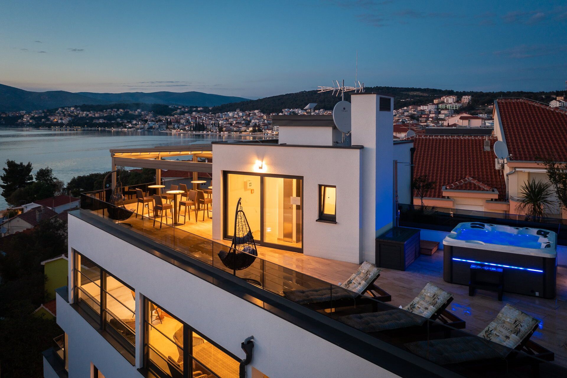 A modern rooftop terrace with a hot tub, seating area, and a view of the city and water.