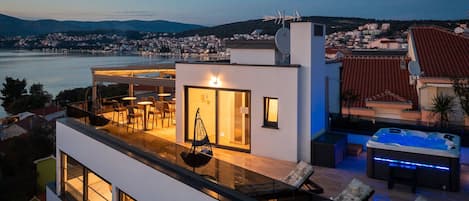 A modern rooftop terrace with a hot tub, seating area, and a view of the city and water.