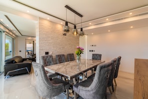 Un espace de salle à manger moderne avec une table en marbre, des chaises à revêtement gris et des luminaires suspendus.