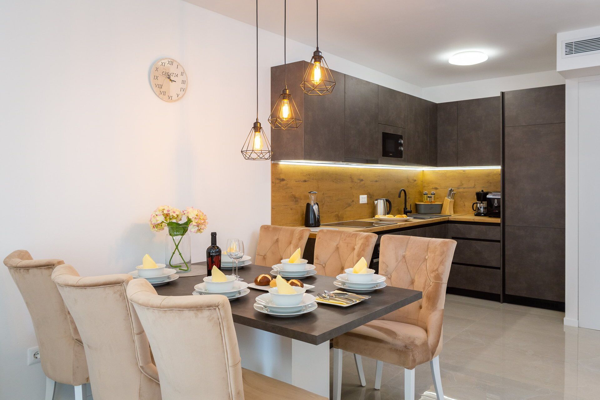 A modern dining area with a dark wooden table, beige upholstered chairs, and pendant lighting.