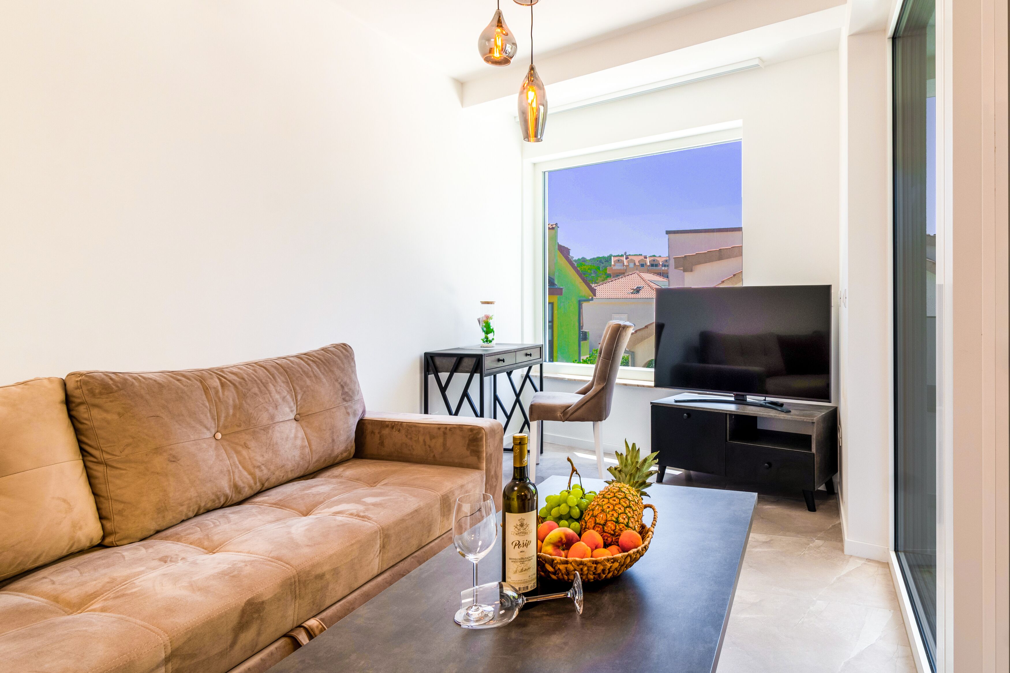 Un salon moderne avec un canapé en cuir, une table basse sur laquelle se trouve un panier de fruits, une bouteille de vin et un téléviseur.