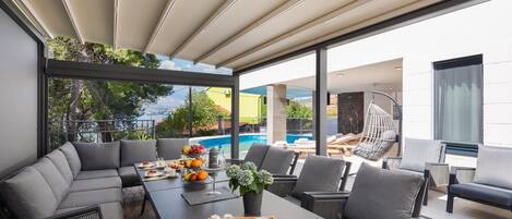 Un área de comedor moderna al aire libre con vista a la piscina, mobiliario gris y un frutero.