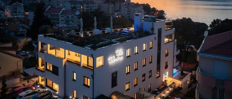 A modern hotel with a rooftop terrace, a pool, and a view of the sea.