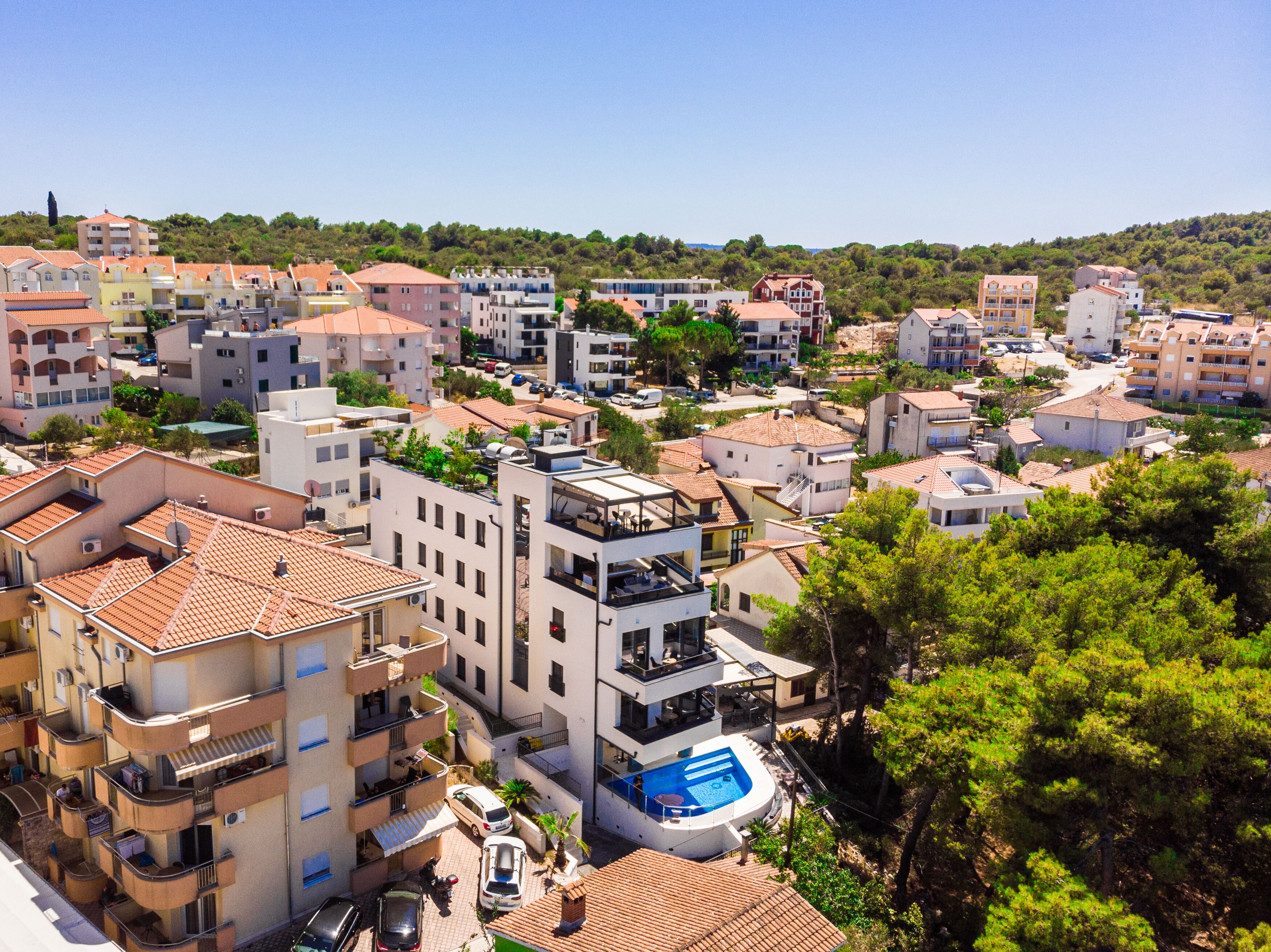 A residential area with multi-story buildings, a swimming pool, and a hilly backdrop.