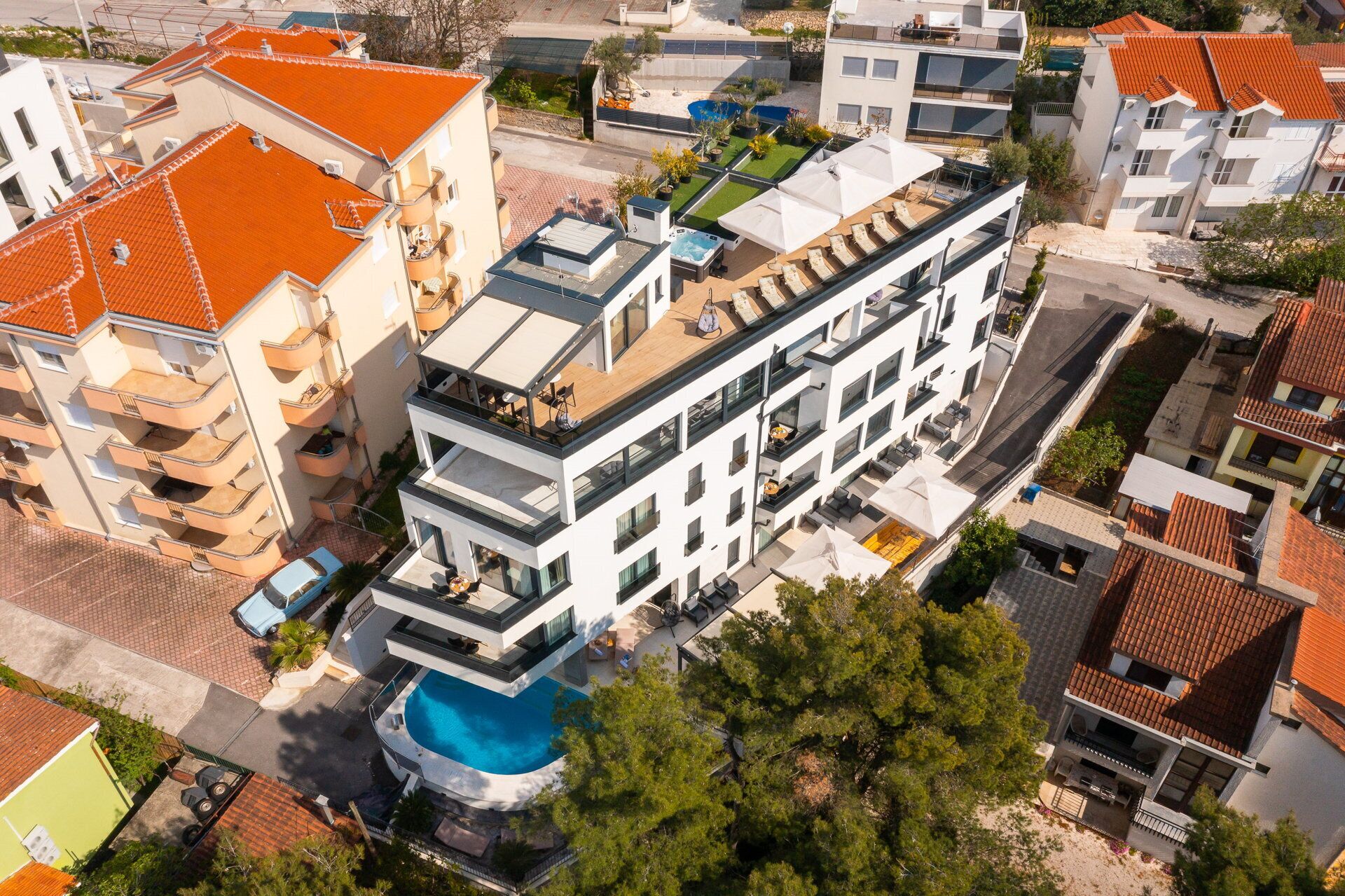 Un hotel de varios pisos con balcones, piscina en la azotea y un jardín.