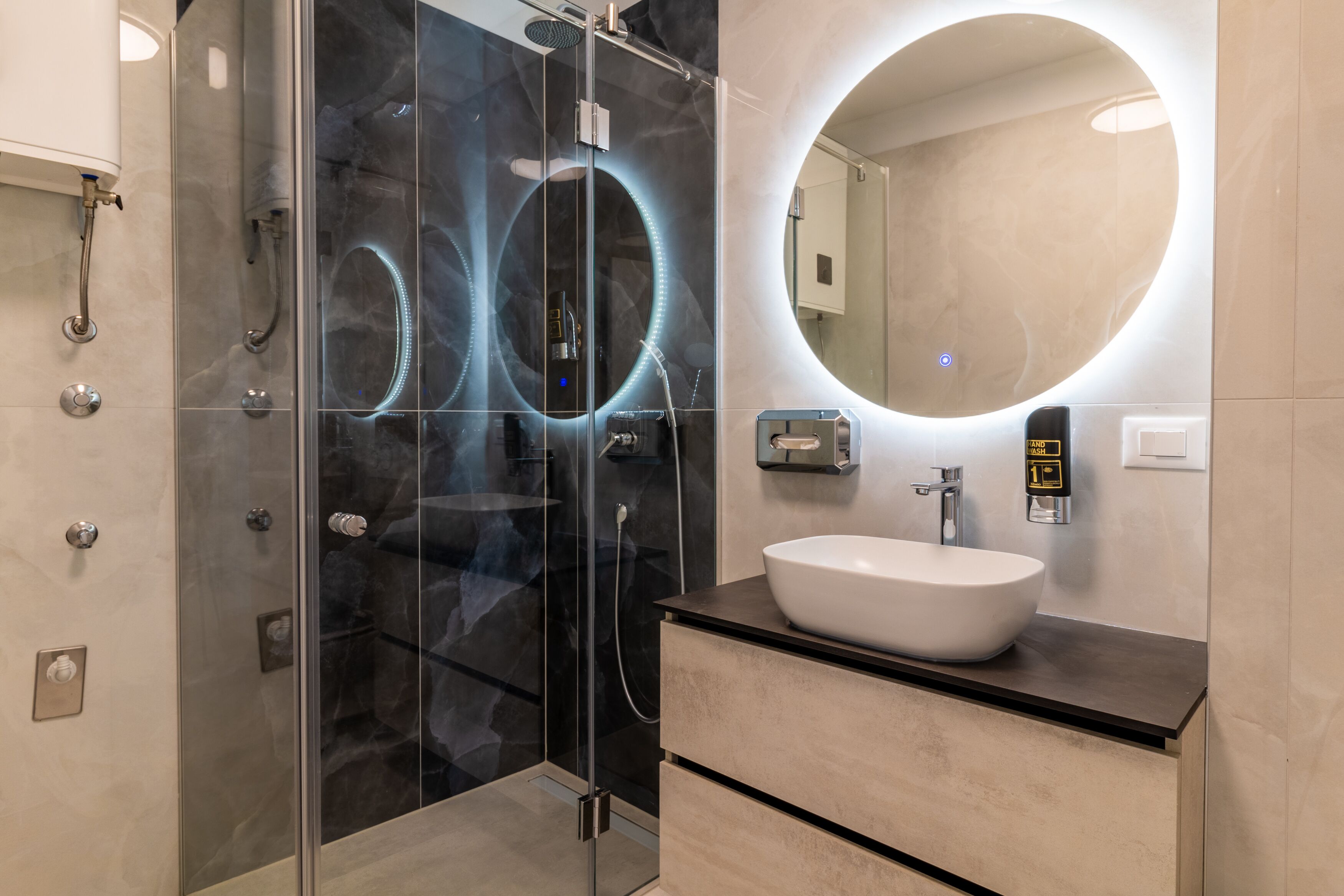 Une salle de bain moderne avec une douche à parois de verre, un miroir rond et un lavabo blanc.