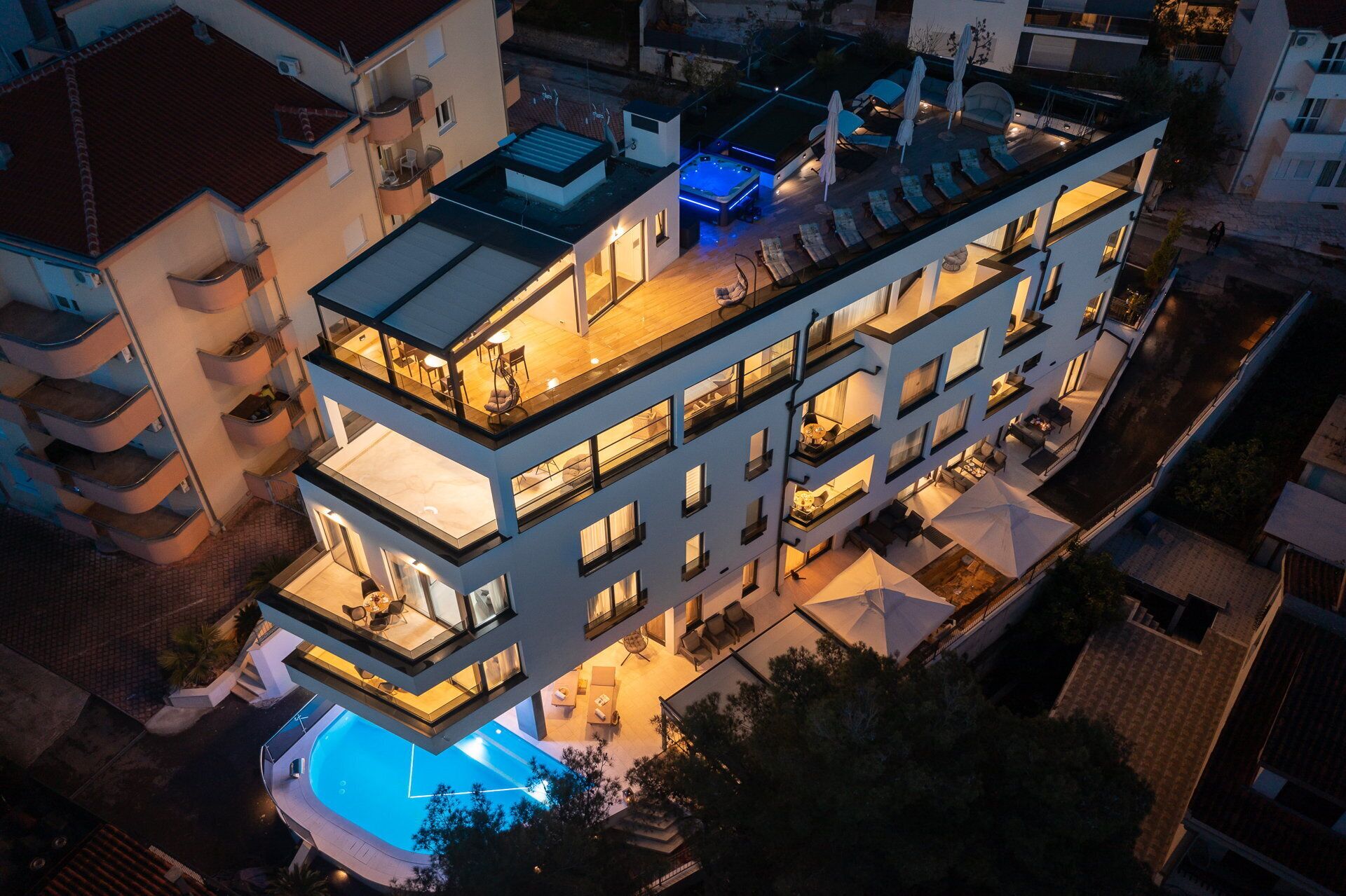 A multi-story hotel with a rooftop pool, outdoor seating, and a jacuzzi.